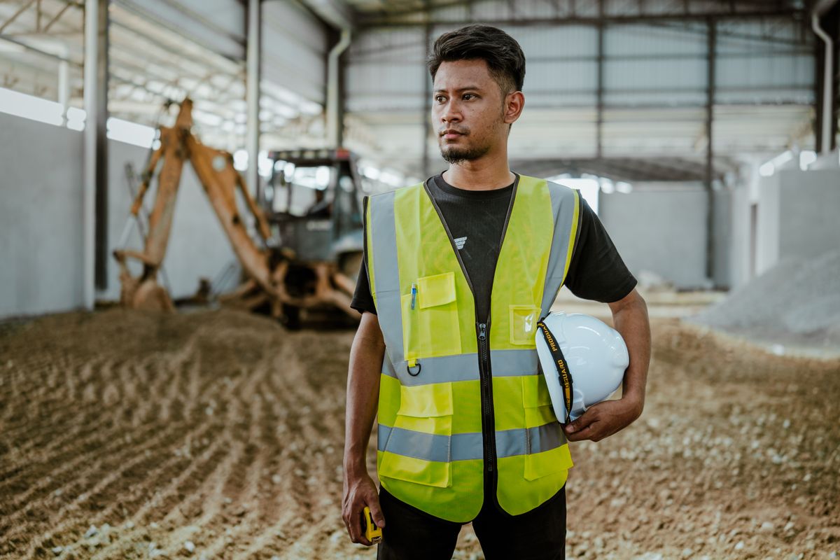 Bauleiter mit Schutzhelm auf einer Baustelle, im Hintergrund ein Bagger