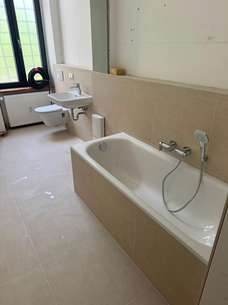 Fertig gefliestes Bad mit Badewanne, Waschtisch, Hänge-WC und großem Sprossenfenster